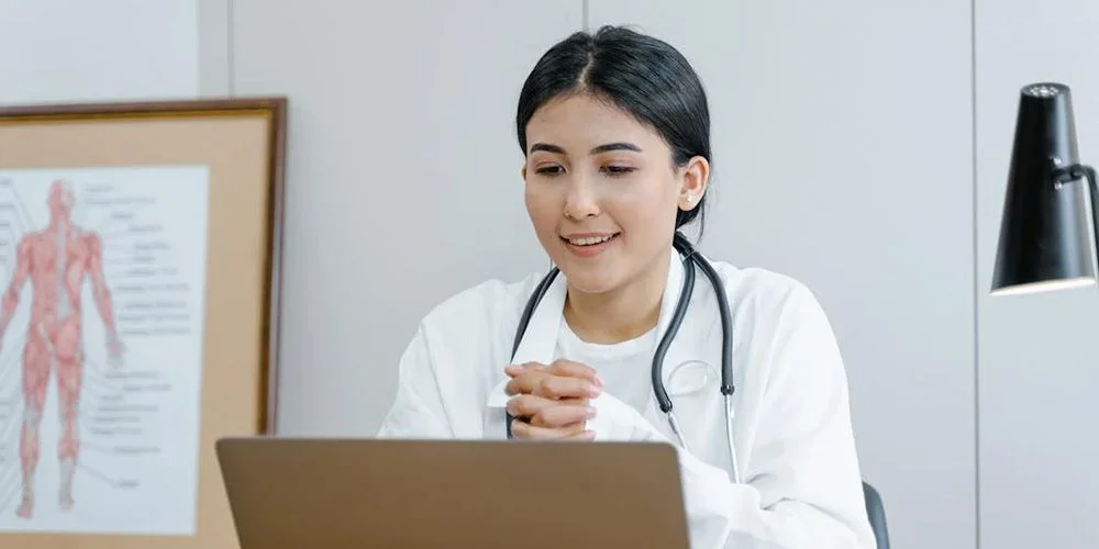 Physician in white coat with stethoscope reviewing job listings on a laptop